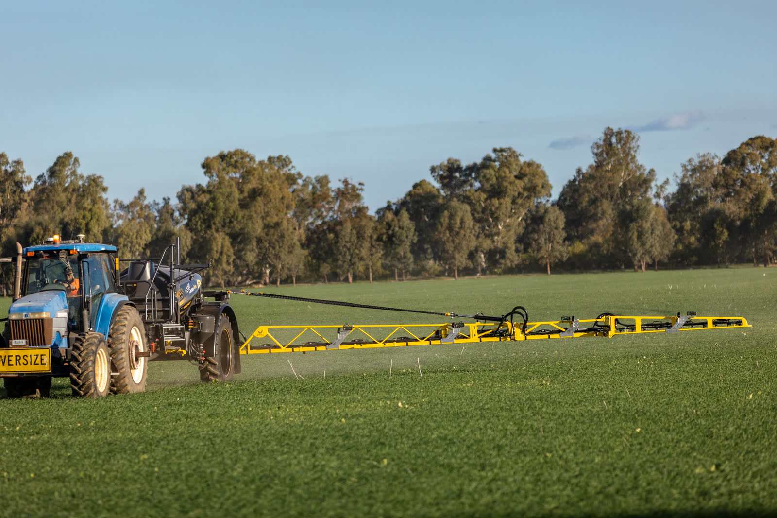 A tractor towing a Stoll CB4 across a paddock, boom out