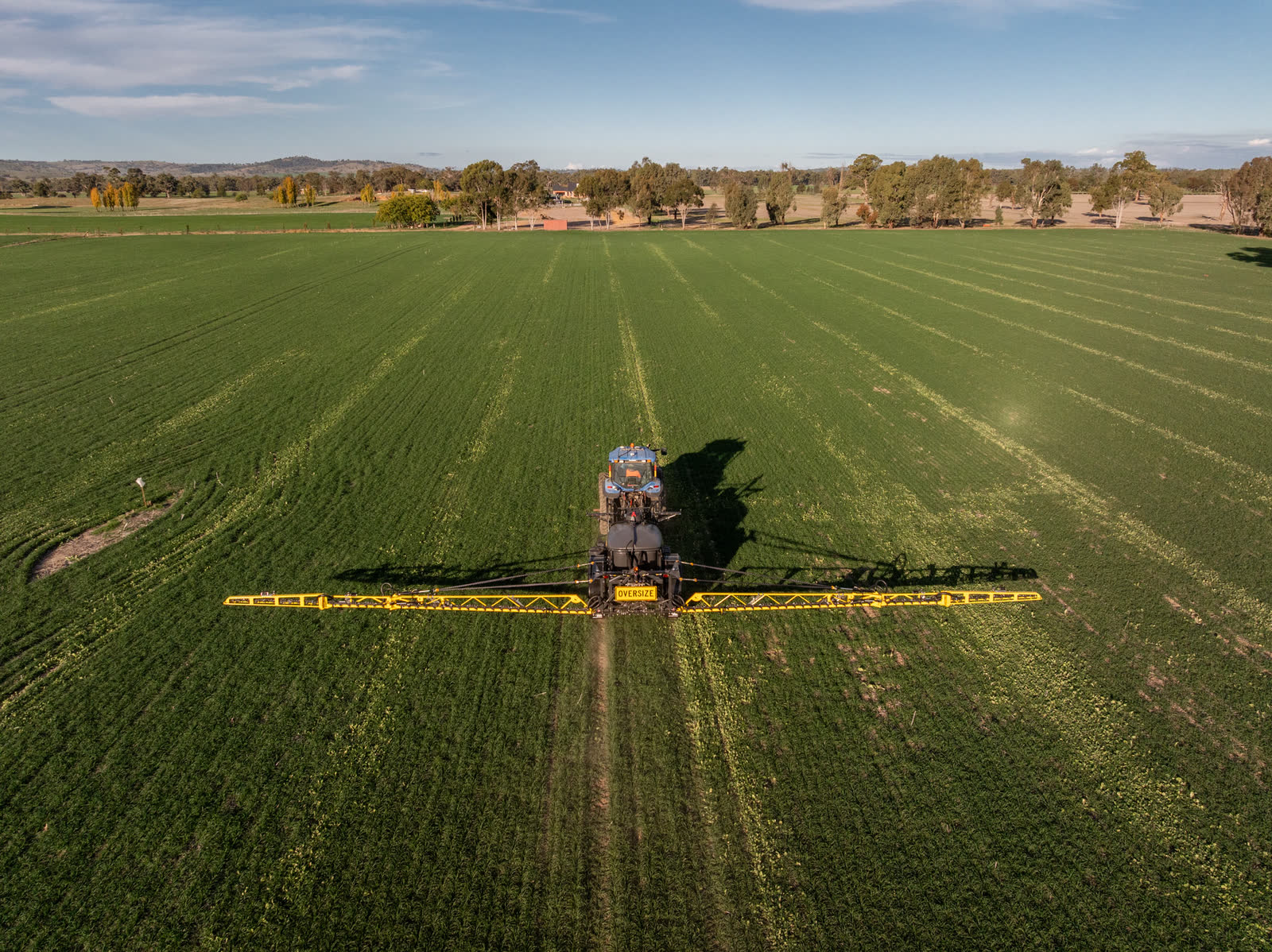 Aerial view of a sprayer working a large green paddock